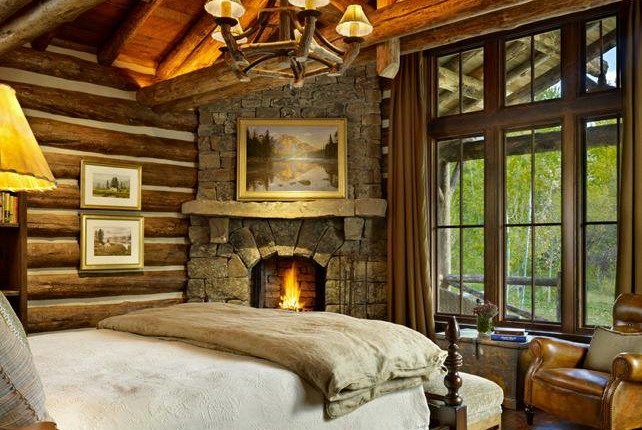 The master bedroom of this mountain cabin home has a beautiful rustic stone fire…