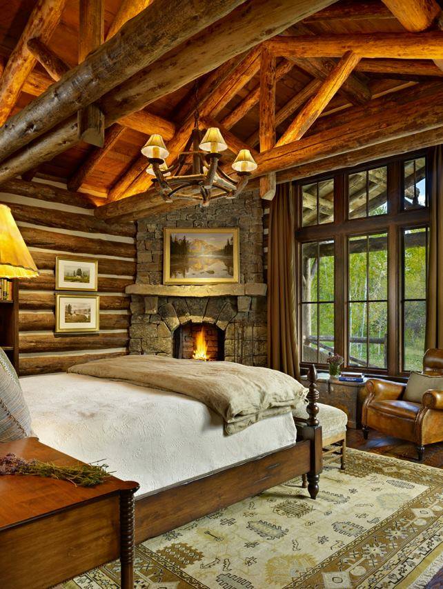 The master bedroom of this mountain cabin home has a beautiful rustic stone fire…