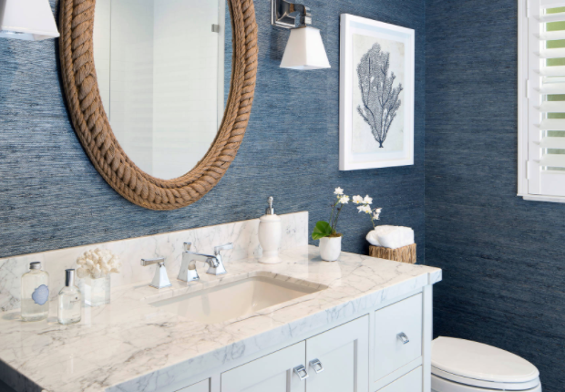 The textured blue grasscloth wallpaper and rope-framed mirror give off a beachy …