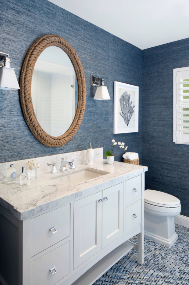 The textured blue grasscloth wallpaper and rope-framed mirror give off a beachy …